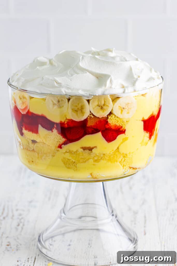Decadent Banana Split Trifle Recipe with Layers of Cream and Fruit 16 Whipped topping spread over sliced bananas in a clear trifle bowl for Banana Split Trifle.