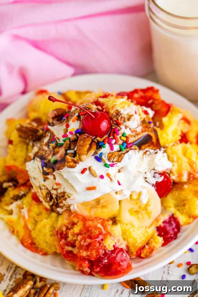 Decadent Banana Split Trifle Recipe with Layers of Cream and Fruit 20 Close-up of Banana Split Trifle on a plate with layers of cake, pudding, strawberry filling, bananas, whipped topping, chocolate sauce, pecans, rainbow sprinkles, and a maraschino cherry.