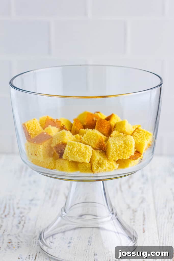 Decadent Banana Split Trifle Recipe with Layers of Cream and Fruit 7 Cubed yellow cake layered in the bottom of a clear trifle bowl for Banana Split Trifle.