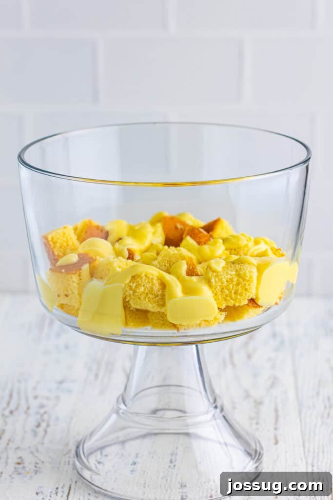 Decadent Banana Split Trifle Recipe with Layers of Cream and Fruit 8 Cubed yellow cake topped with vanilla pudding in a clear trifle bowl for Banana Split Trifle.