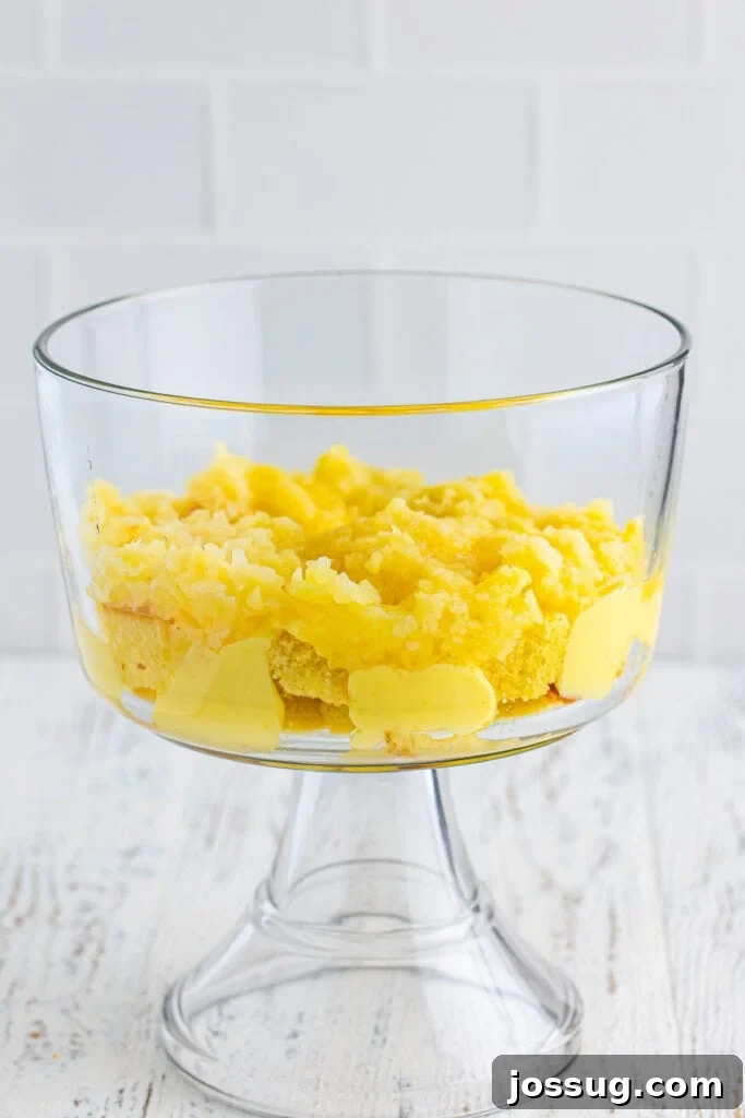 Decadent Banana Split Trifle Recipe with Layers of Cream and Fruit 9 Layer of crushed pineapple spread over cake and pudding in a clear trifle bowl for Banana Split Trifle.