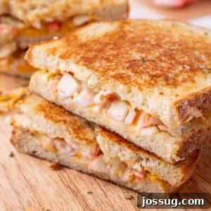 Cheesy Crab Melt: Seafood Grilled Cheese Sandwich Recipe 15 Square image of stacked Cheesy Crab Melt sandwich halves on a wooden cutting board