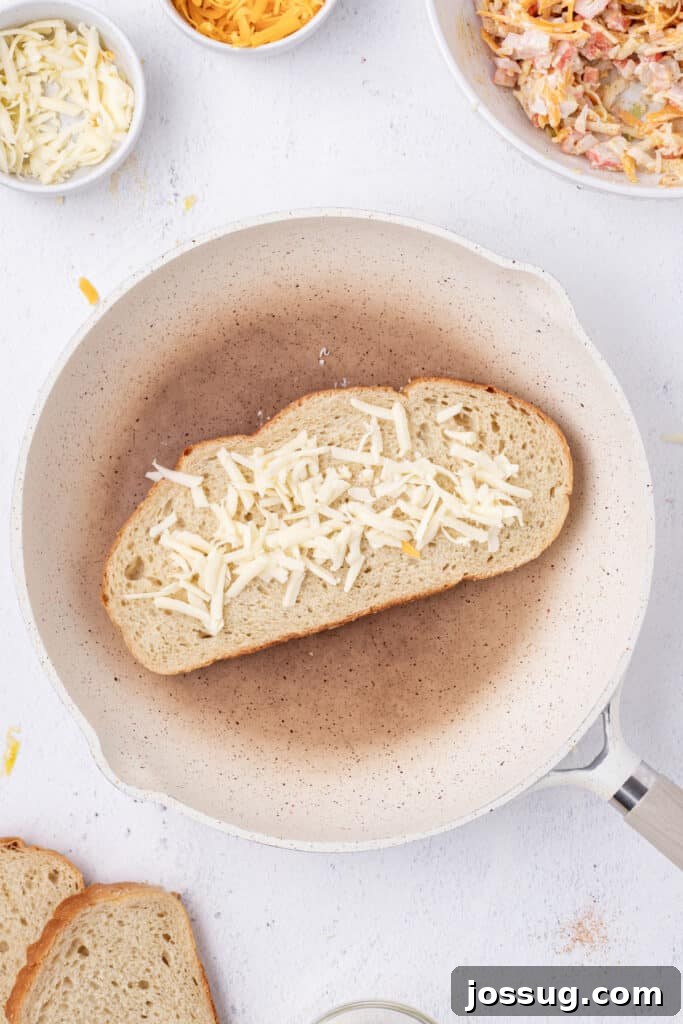 Cheesy Crab Melt: Seafood Grilled Cheese Sandwich Recipe 8 Shredded Gruyere cheese sprinkled onto a slice of sourdough bread in a skillet