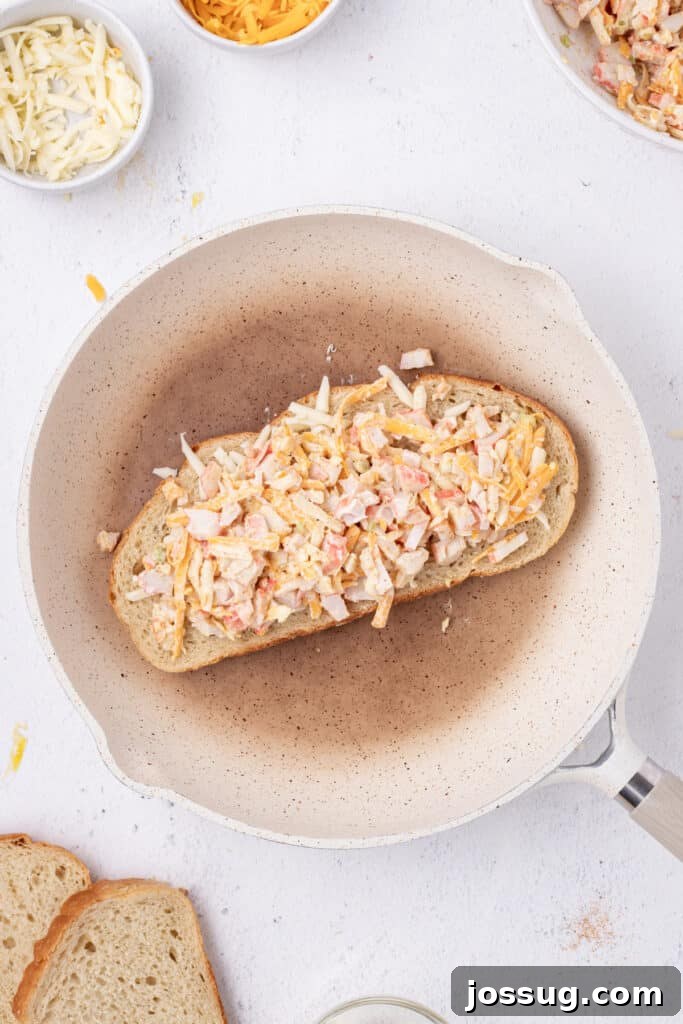 Cheesy Crab Melt: Seafood Grilled Cheese Sandwich Recipe 9 Cheesy crab filling spread over cheese on a slice of sourdough bread in a skillet
