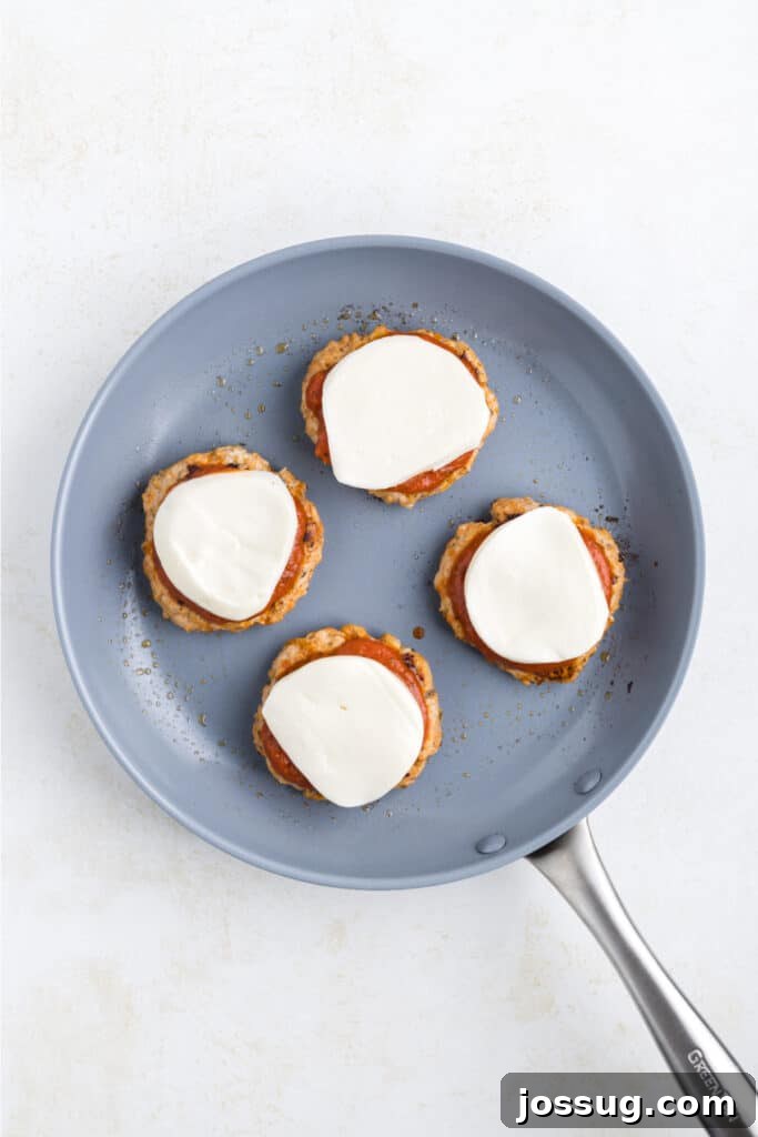 Crispy Chicken Parmesan Burgers with Marinara and Mozzarella 11 Chicken Parm Burger patties topped with marinara sauce and mozzarella cheese in a skillet
