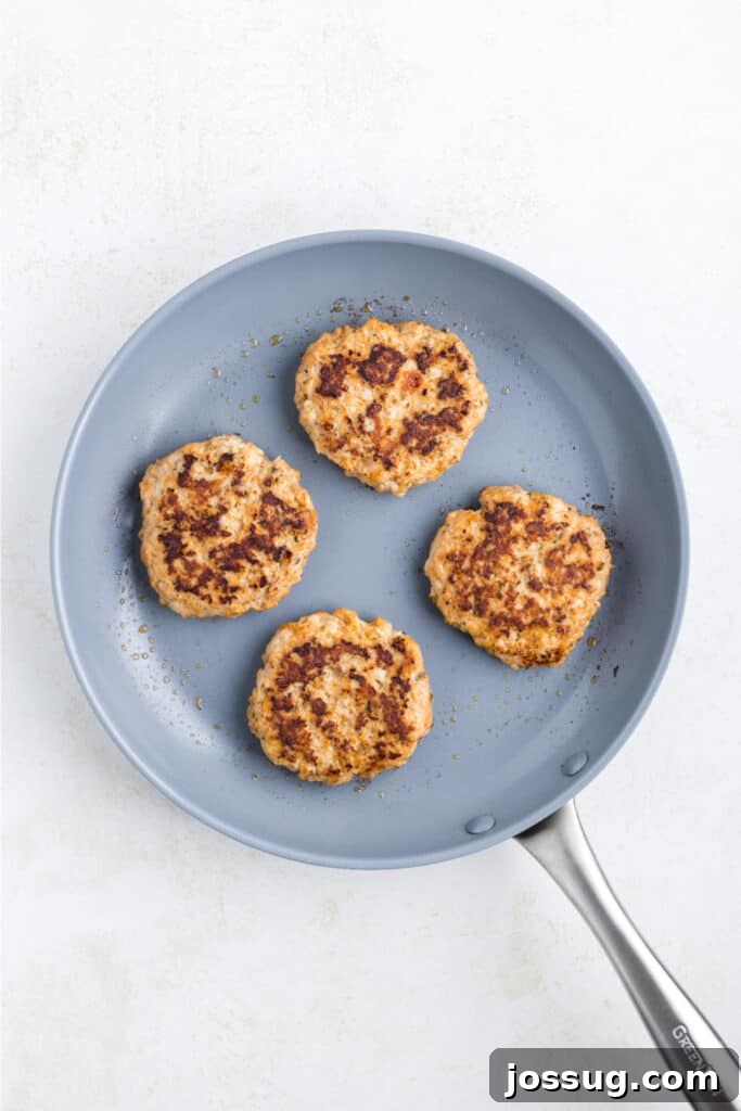 Crispy Chicken Parmesan Burgers with Marinara and Mozzarella 9 Chicken Parm Burger patties cooking in a skillet