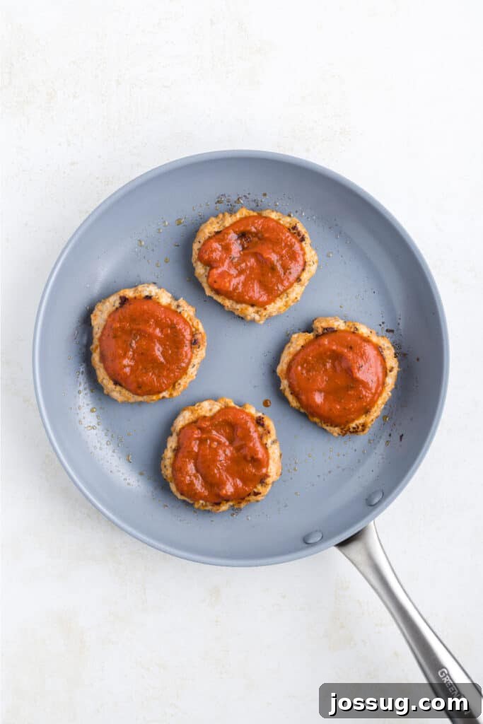 Crispy Chicken Parmesan Burgers with Marinara and Mozzarella 10 Cooked Chicken Parm Burger patties topped with marinara sauce in a skillet