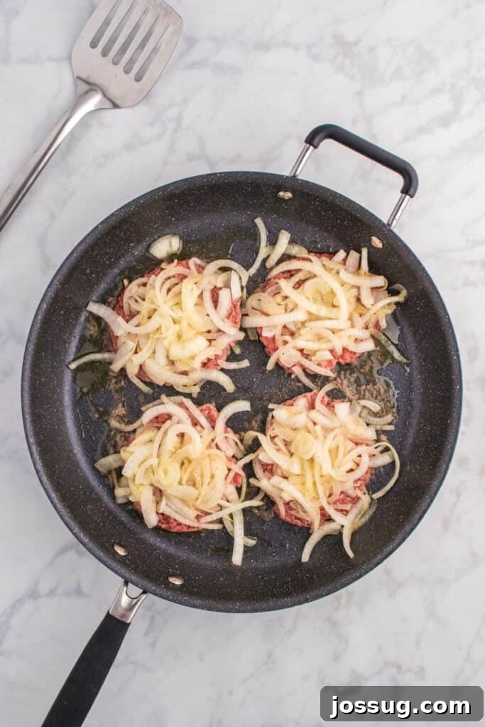 Oklahoma Onion Smash Burger Recipe with Caramelized Onions 7 Thinly sliced onions piled onto smashed burger patties.