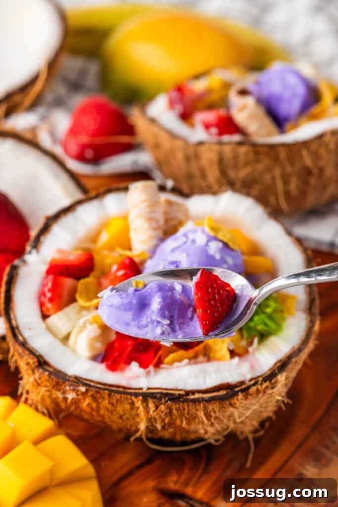Halo-Halo: Authentic Filipino Shaved Ice Recipe 9 Spoonful of Halo Halo with creamy ube ice cream and fresh strawberry above a coconut bowl filled with tropical toppings.