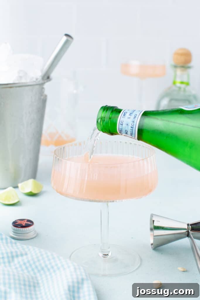 Topping a Paloma Cocktail with sparkling water before serving.