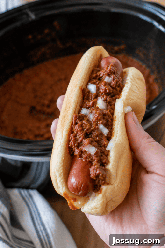 Slow Cooker Hot Dog Chili with Homemade Chili Sauce 9 Hand holding a chili dog topped with homemade hot dog chili and diced onions.