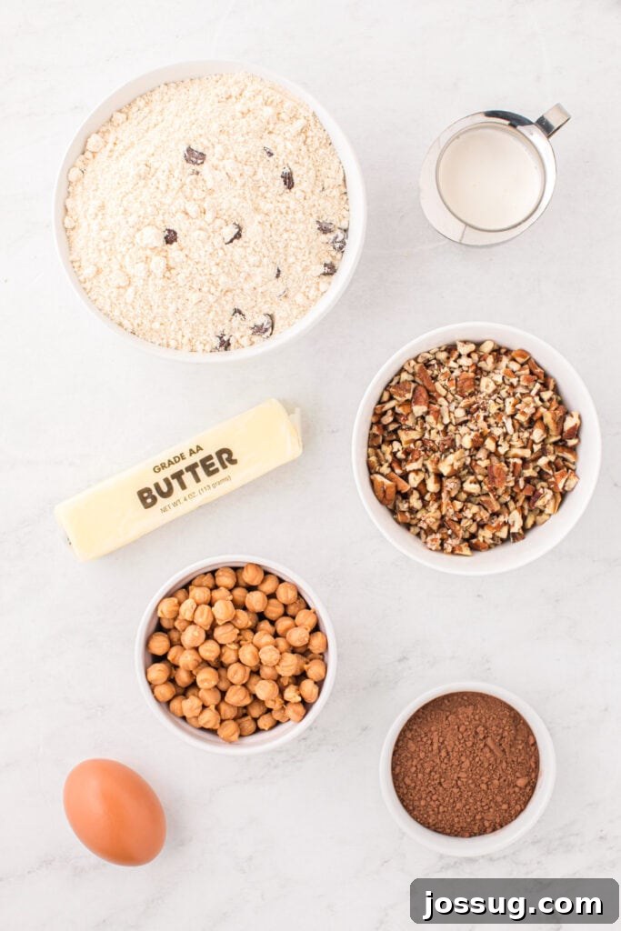 Ingredients for Easy Turtle Cookies including chocolate chip cookie mix, cocoa powder, butter, egg, heavy cream, chopped pecans, and caramel bits arranged on a countertop.