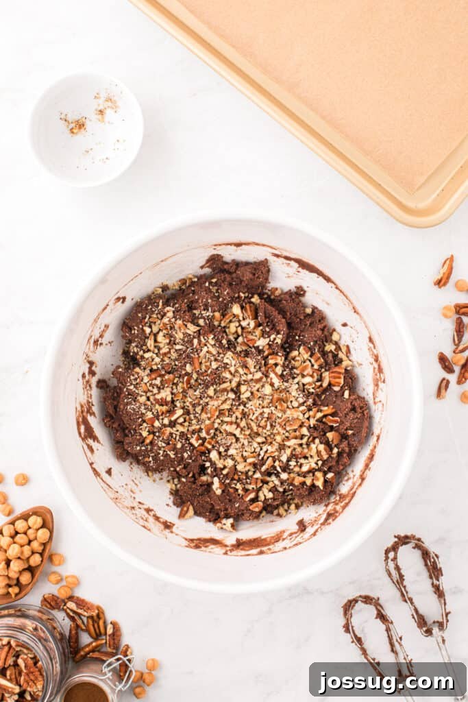 Chopped pecans being added to rich chocolate cookie dough for Easy Turtle Cookies.