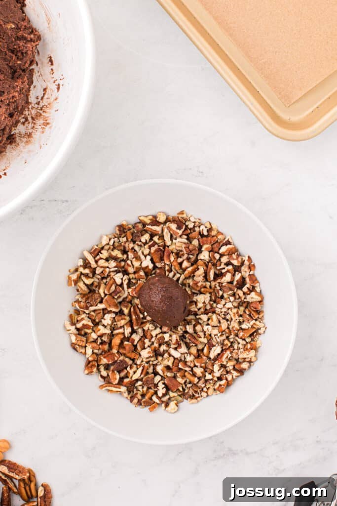 Ball of Easy Turtle Cookie dough rolled in chopped pecans before baking.