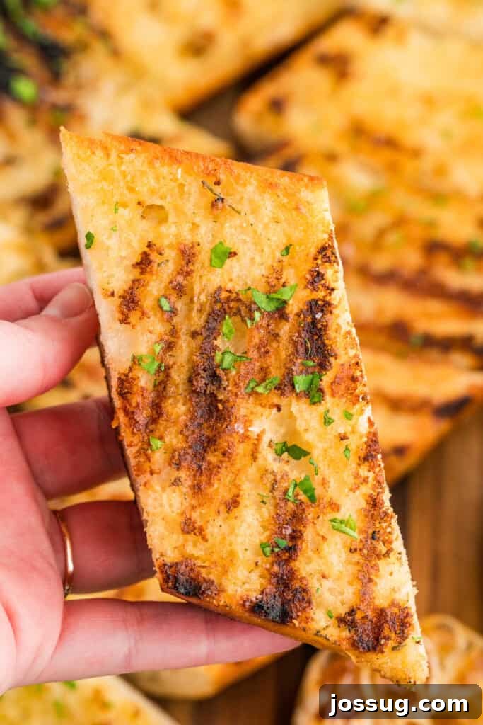 Hand holding a slice of Grilled Garlic Bread showing the crispy grilled surface and buttery interior.