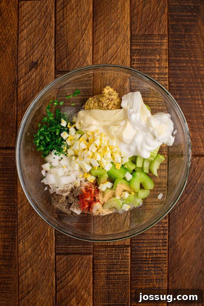 Southern-Style Sweet Potato Salad Recipe 6 Creamy Sweet Potato Salad dressing ingredients with chopped eggs, celery, onion, parsley, mustard, and seasonings in a mixing bowl