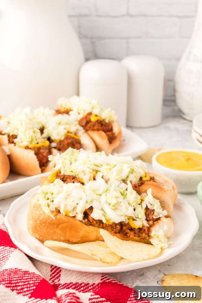 Plate with two Carolina Dogs topped with homemade hot dog chili, creamy slaw, and chopped onions, served with potato chips.