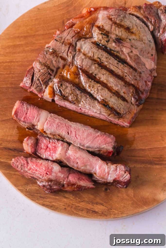 Smoked ribeye steak with grill marks and several thick slices arranged on a wooden cutting board.