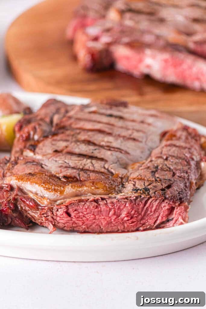 Smoked Ribeye with a seared exterior and juicy pink center served on a white plate.