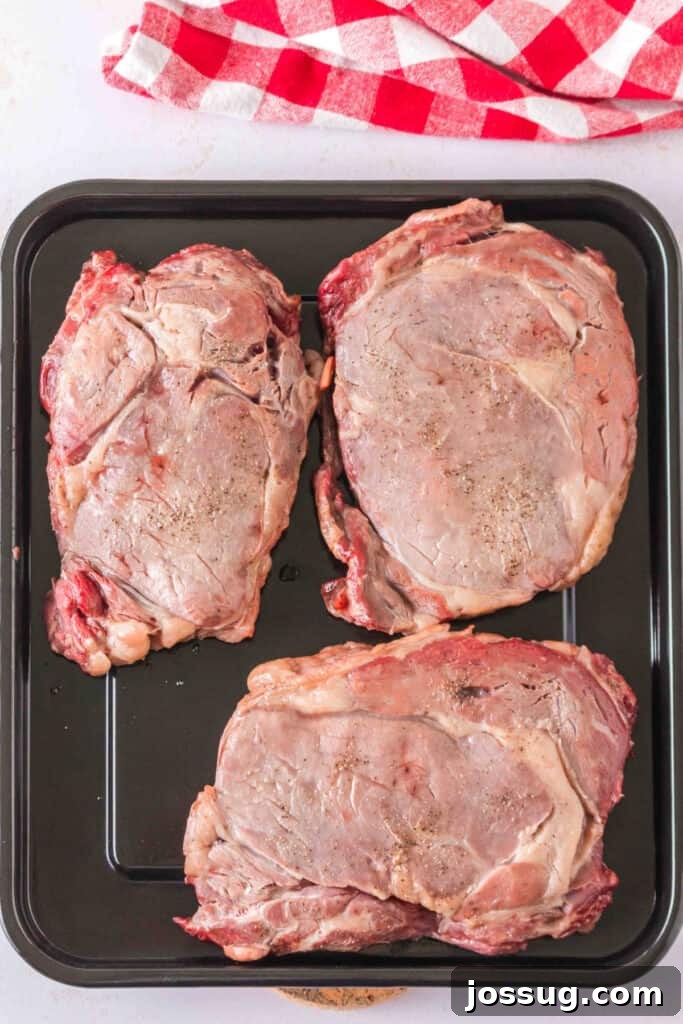 Three partially cooked ribeye steaks resting on a tray before searing.