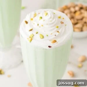 Pistachio milkshake topped with whipped cream and chopped pistachios in a square food photo