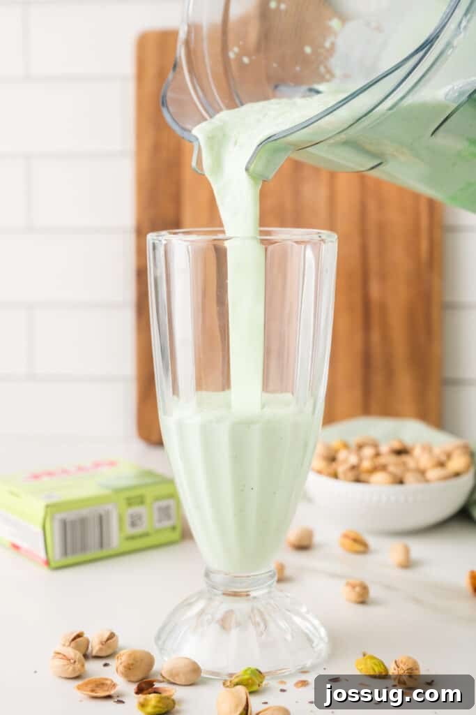 Creamy pistachio milkshake being poured from a blender into a tall glass