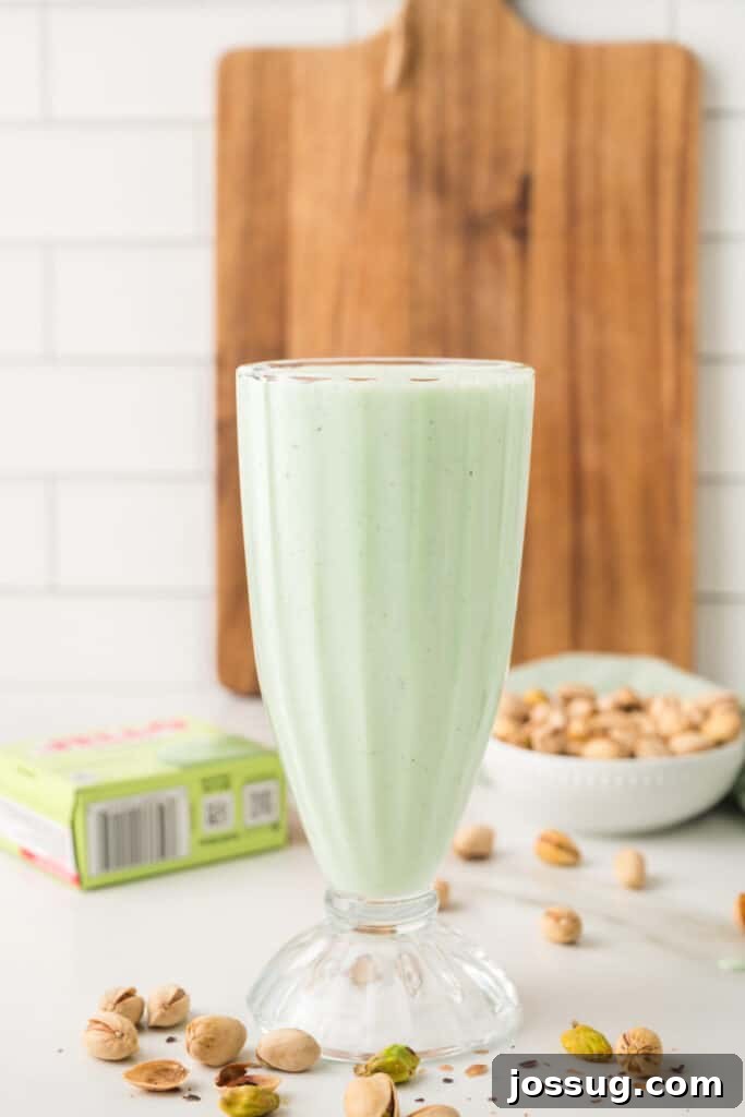 Freshly blended pistachio milkshake in a tall glass with pistachios scattered around it
