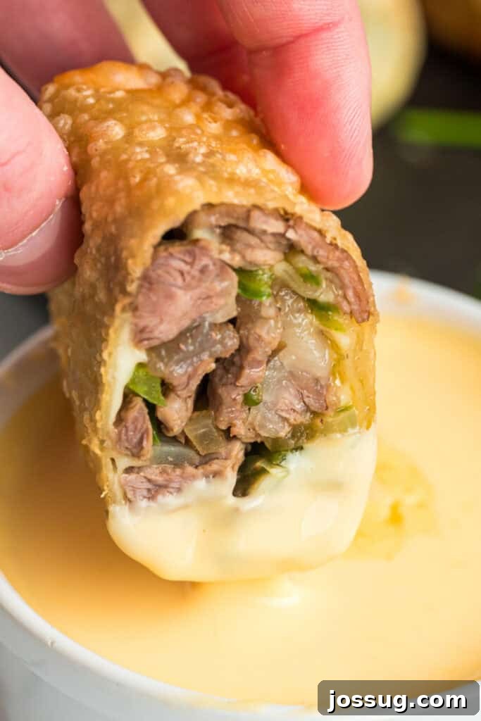 Crispy steak and cheese egg roll dipped into creamy cheese sauce