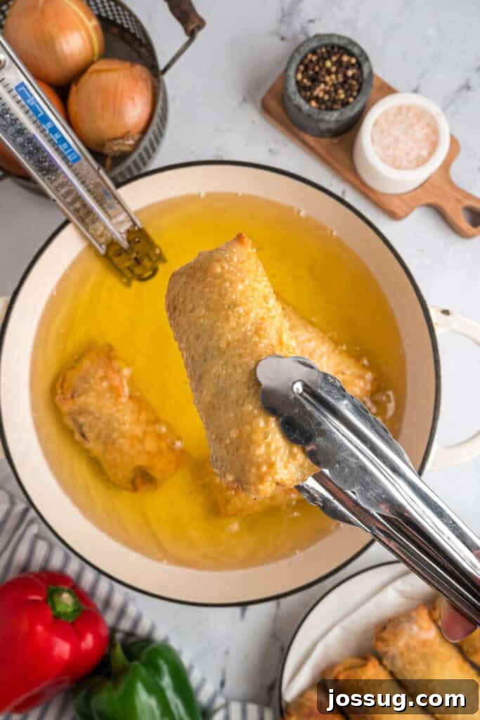 Golden brown Philly Cheesesteak Egg Roll being removed from the hot frying oil with tongs