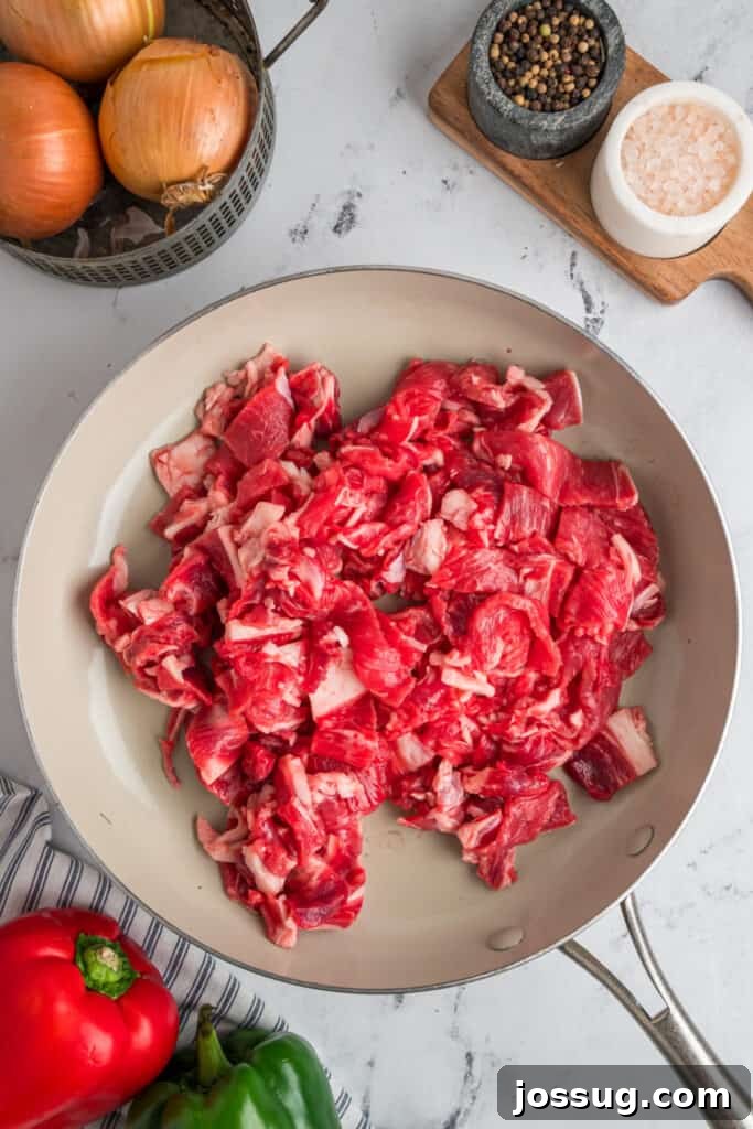 Thinly sliced steak cooking in a large skillet for Philly Cheesesteak Egg Rolls