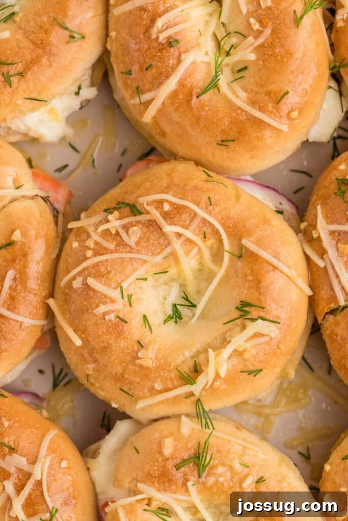 Baked Bagel and Smoked Salmon Sliders 18 Close-up of golden baked mini bagel sliders topped with Parmesan cheese and fresh dill
