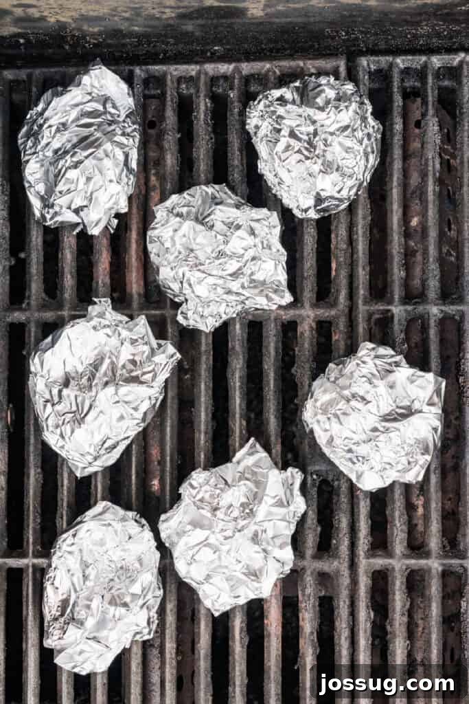 Foil-wrapped garlic bulbs cooking over indirect heat on the grill